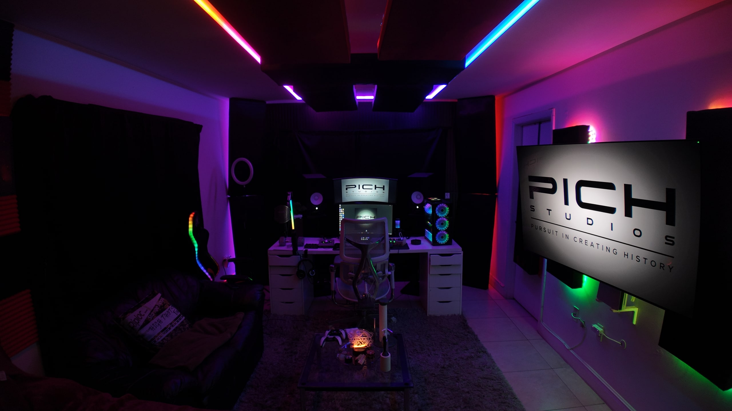 Wide view of the PICH studio with purple and blue lighting, recording desk, seating and the PICH logo displayed on the TV